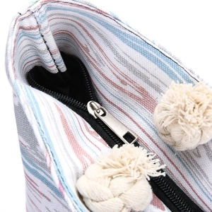 Detail of silver metal zipper and beige tassel on a striped canvas tote bag