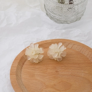 Detail view of matte cream flower earrings with S925 silver needles on a wood tray