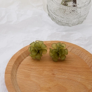 Detail view of frosted green floral earrings on a wooden tray with a minimalist aesthetic