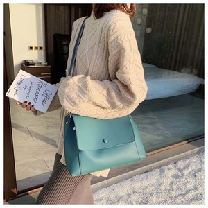 Detail of teal faux leather crossbody bag with geometric woven strap on a person