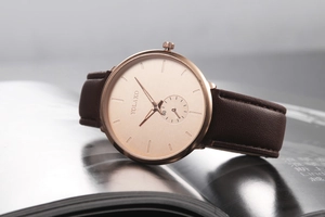 Macro view of rose gold men's watch with brown leather strap on a magazine background
