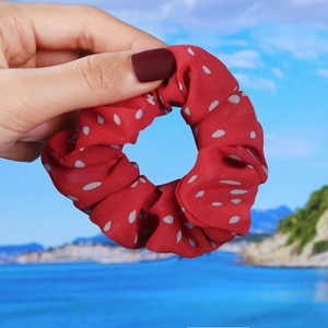 Detail of red chiffon scrunchie with white polka dots held against a coastal beach background