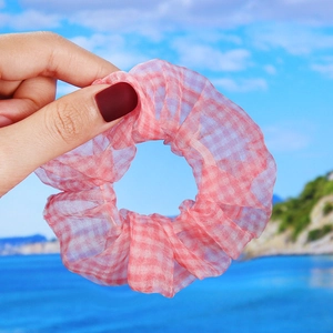 Pink checkered organza hair scrunchie with daisy pattern held against a beach background