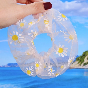 Detailed view of white tulle hair scrunchie with yellow daisy print held by a hand