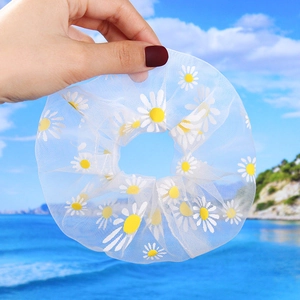 Detailed view of daisy pattern on lightweight white organza scrunchie held by hand