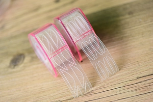 Detailed view of mesh lace double eyelid tapes with pink dispensers on a wooden desk
