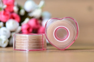 Lace eyelid tape rolls with heart-shaped dispenser shown on a rustic wooden background