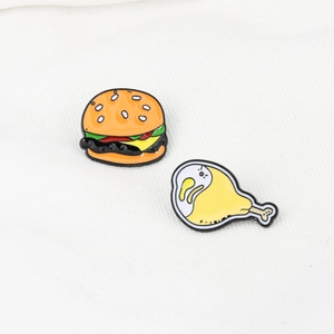 Detail shot of cartoon burger and chicken leg enamel pins on white textured fabric
