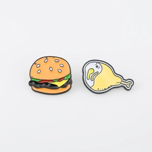 Detail of cartoon enamel pins featuring a classic burger and yellow bird chicken leg design