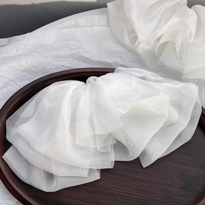 Detail of multi-layered white chiffon bow hair clip with translucent organza on wood tray