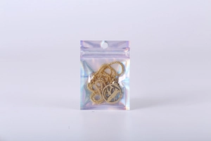 Detail view of a gold chain necklace with a round pendant inside a holographic ziplock bag