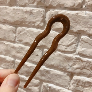 Macro detail of wave-shaped U-shaped resin hair pin in caramel brown finish