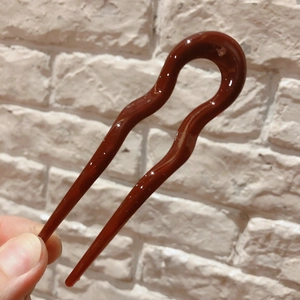 Detail showing smooth brown resin U-shaped hair pin with a polished glossy finish