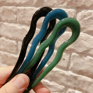 Close-up of wavy U-shaped resin hair pins in black, teal, and dark green colors
