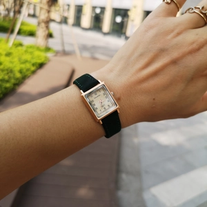 Detail view of square gold watch with black leather strap on female wrist in outdoor setting