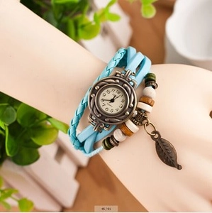Dettaglio di un orologio vintage in pelle con ciondoli in bronzo e pendente foglia