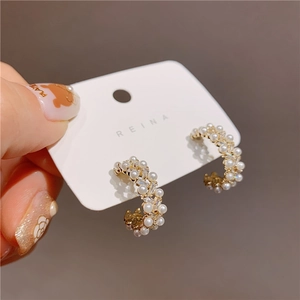 Detail of C-shaped gold earrings featuring embedded pearls and shimmering zircons