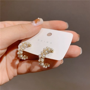 Detail of C-shaped gold earrings featuring inlaid pearls and rectangular zircons