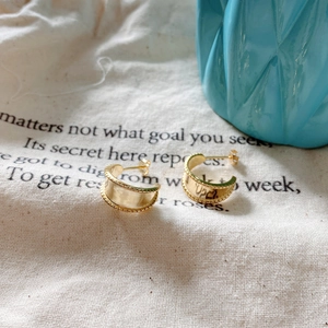 Detail view of gold C-shape stud earrings with textured edges on natural linen fabric