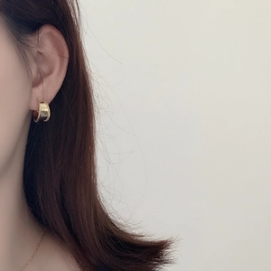 Close-up of gold wide-surface hoop earrings with beaded edges worn on the ear