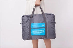 Detail of grey foldable travel bag with blue zipper pocket and city names printed