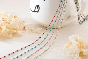 Detail of silver stainless steel chain featuring colorful enamel beads on a white cup