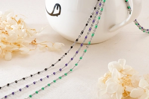 Detail view of colorful resin beads on minimalist steel necklaces draped on a white cup