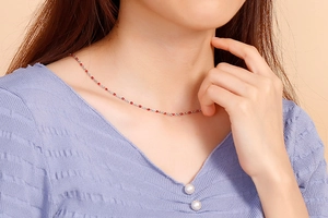 Detail of twisted silver chain necklace with red bead accents on model neck