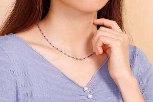 Close-up of a delicate steel necklace with small blue beads worn on a neck