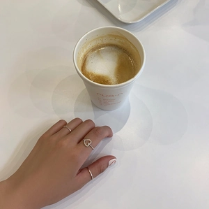 Detail shot of heart-shaped silver ring and thin bands worn in a cozy cafe setting