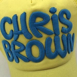 Detailed close-up of 3D blue embroidery 'CHRIS BROWN' on a yellow cotton baseball cap