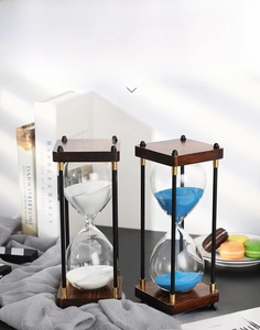 Detail of vintage wooden hourglass with blue and white sand on a cozy desk setting