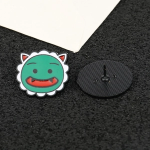 Detail of green enamel monster badge with red mouth and black rubber pin back on black background