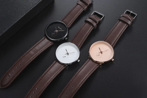 Three men's quartz watches with leather straps in black, white, and pink dials on dark background