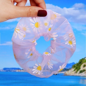 Detailed texture of lavender daisy print mesh hair scrunchie held against blue sky