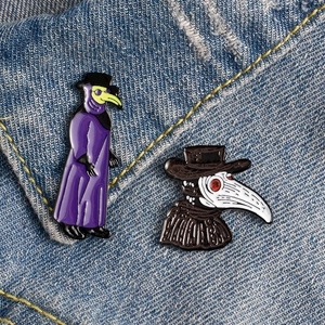 Macro shot of two plague doctor enamel pins with colorful masks on blue denim fabric