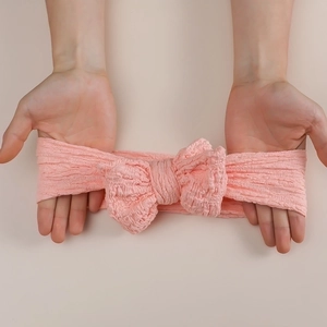 Pink oversized bow baby headband in stretchy crinkle fabric shown being stretched