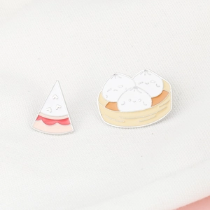 Detailed view of cute enamel pins featuring a cartoon cake slice and steamed buns in a basket