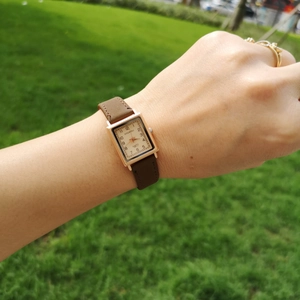 Close-up of a square rose gold watch with brown leather strap worn on a wrist outdoors