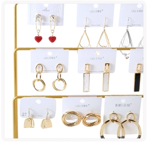 Macro view of gold-tone earrings with red heart and leaf charms on metal display rack