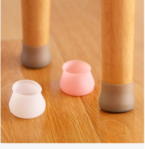 Silicone chair leg protectors in white, pink, and grey on a light wood floor surface