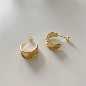 Detail of gold C-shaped wide stud earrings with vintage engraved texture on a light background