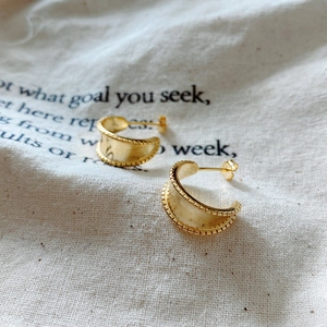 Macro detail of gold half-hoop earrings with beaded edges on white linen fabric