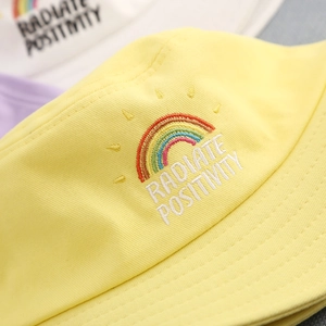 Close-up of rainbow embroidery and text on yellow cotton sun hat for children