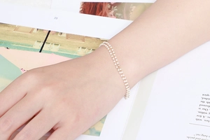 Détail d'un bracelet doré à deux rangs en titane avec perles blanches au poignet