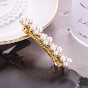 Close-up of elegant gold hair clip with various white pearls on a ceramic dish