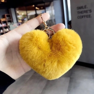 Close-up of fluffy yellow heart plush keychain with golden metal ring held by hand