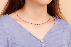 Close-up of minimalist titanium steel necklace with red resin beads on model neck