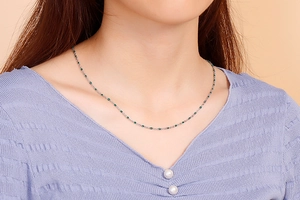Detailed view of dainty silver chain necklace with green resin beads worn by a model