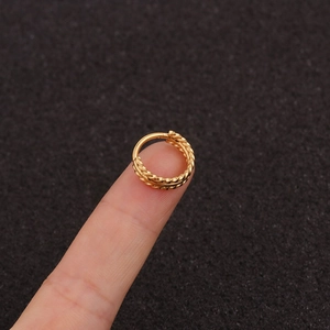 Macro detail of golden triple-row twisted rope texture earring on a finger